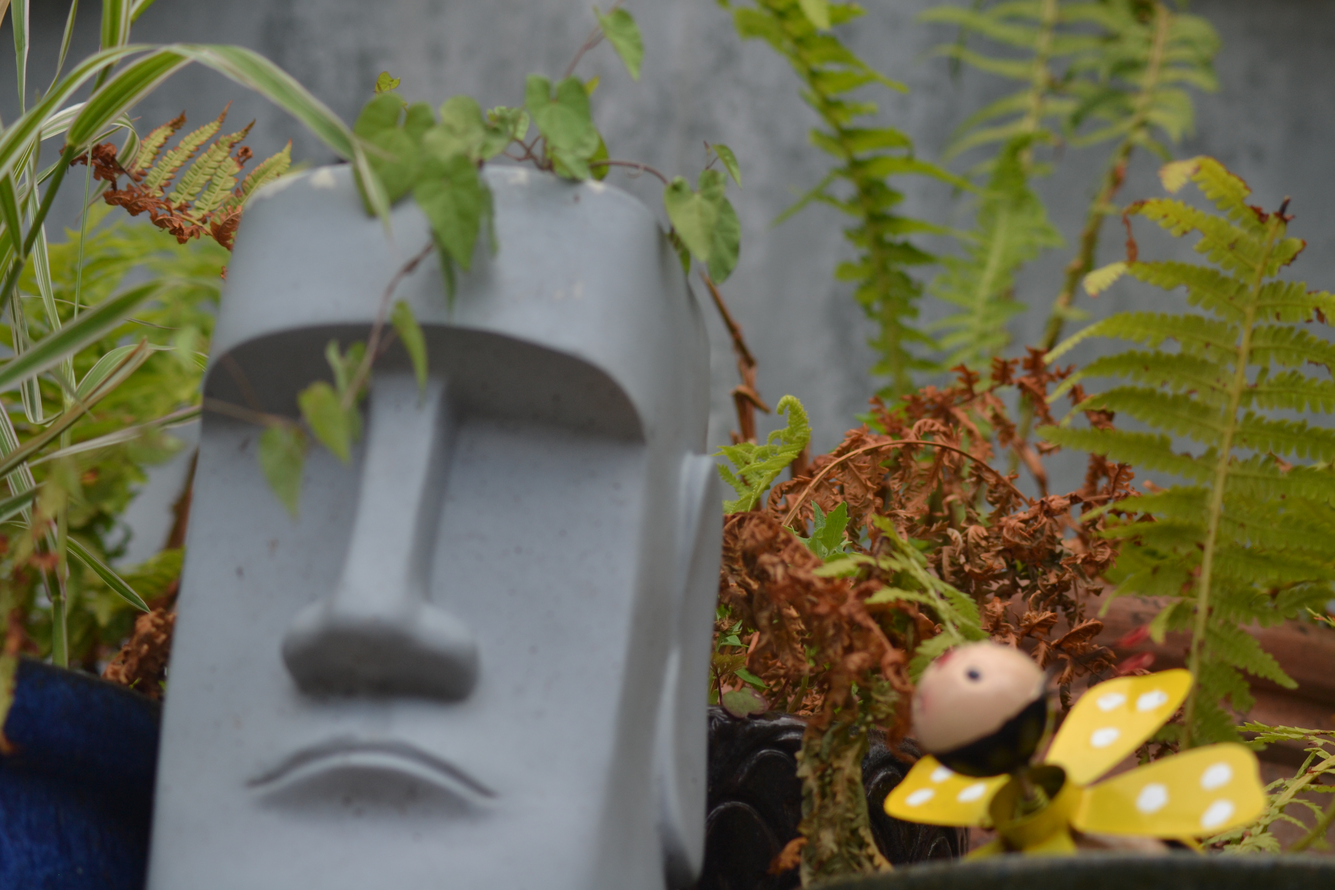 A stone head with grass coming out of its head, and a fake butterfly beside it.